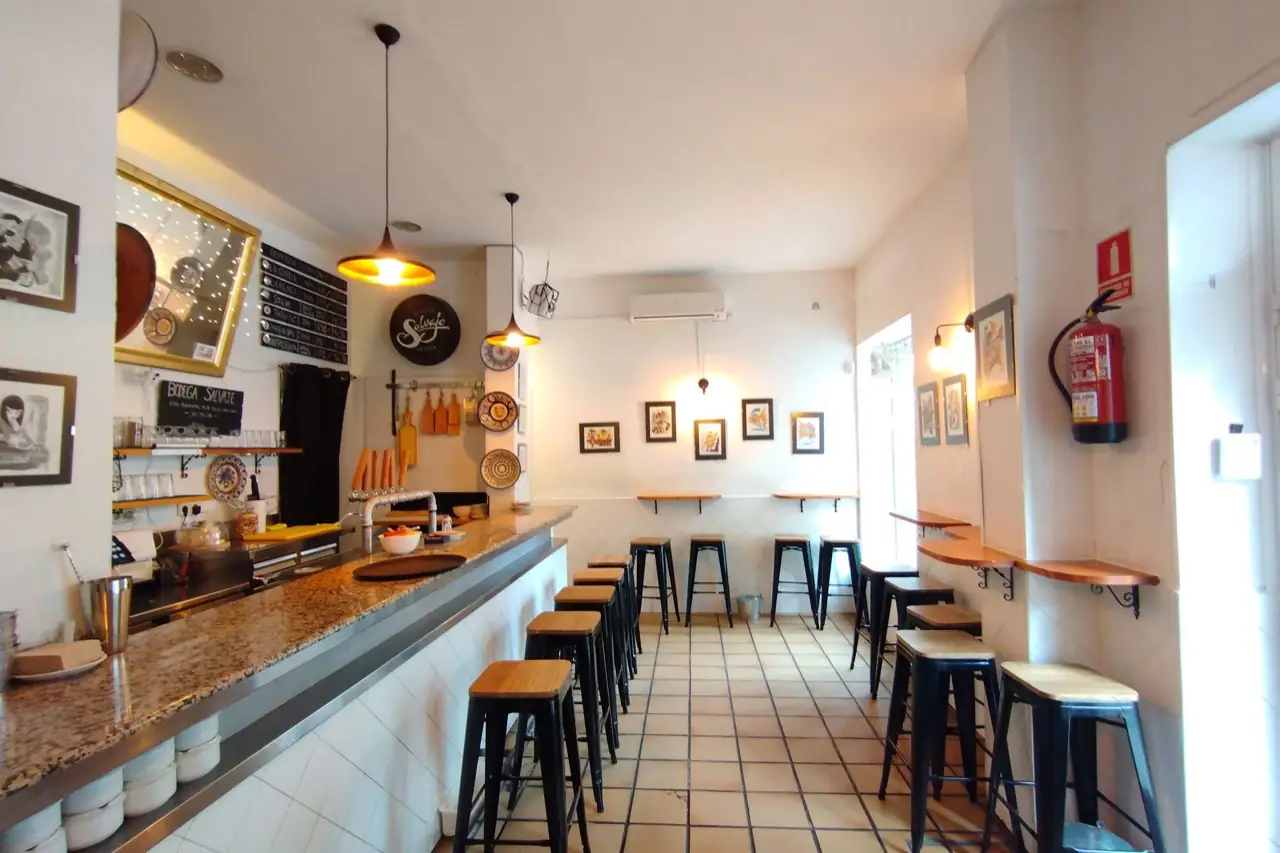 Narrow tapas bar with a granite counter, beer taps, a 'Bodega Salvaje' chalkboard, black metal stools with wood seats and framed art on white walls