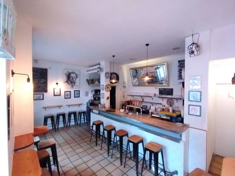 Wide view of the Bodega Salvaje bar with a charcoal portrait sketch on the wall, pendant lights and stools along the counter