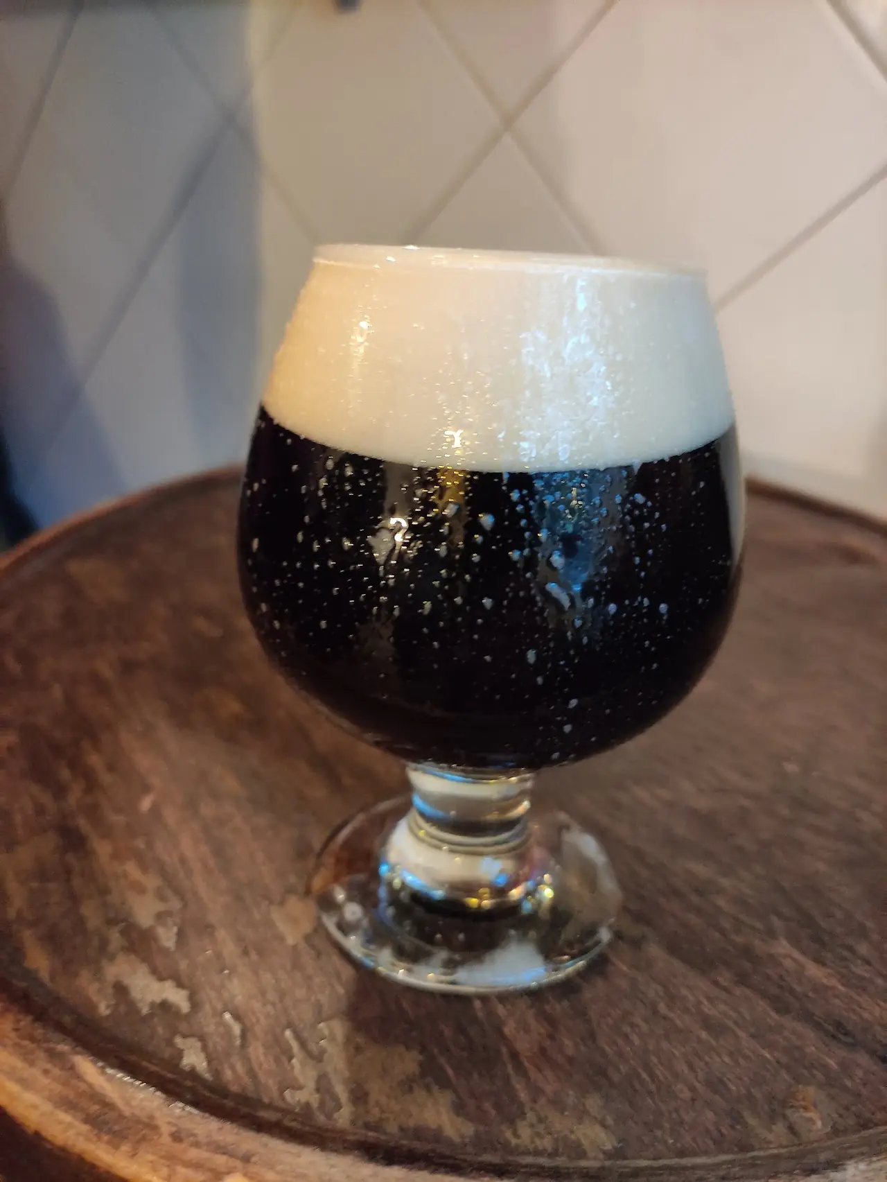 A snifter glass of dark beer with a thick foam head on a wooden table.