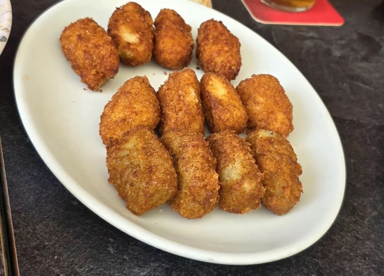 An oval white plate of golden croquetas