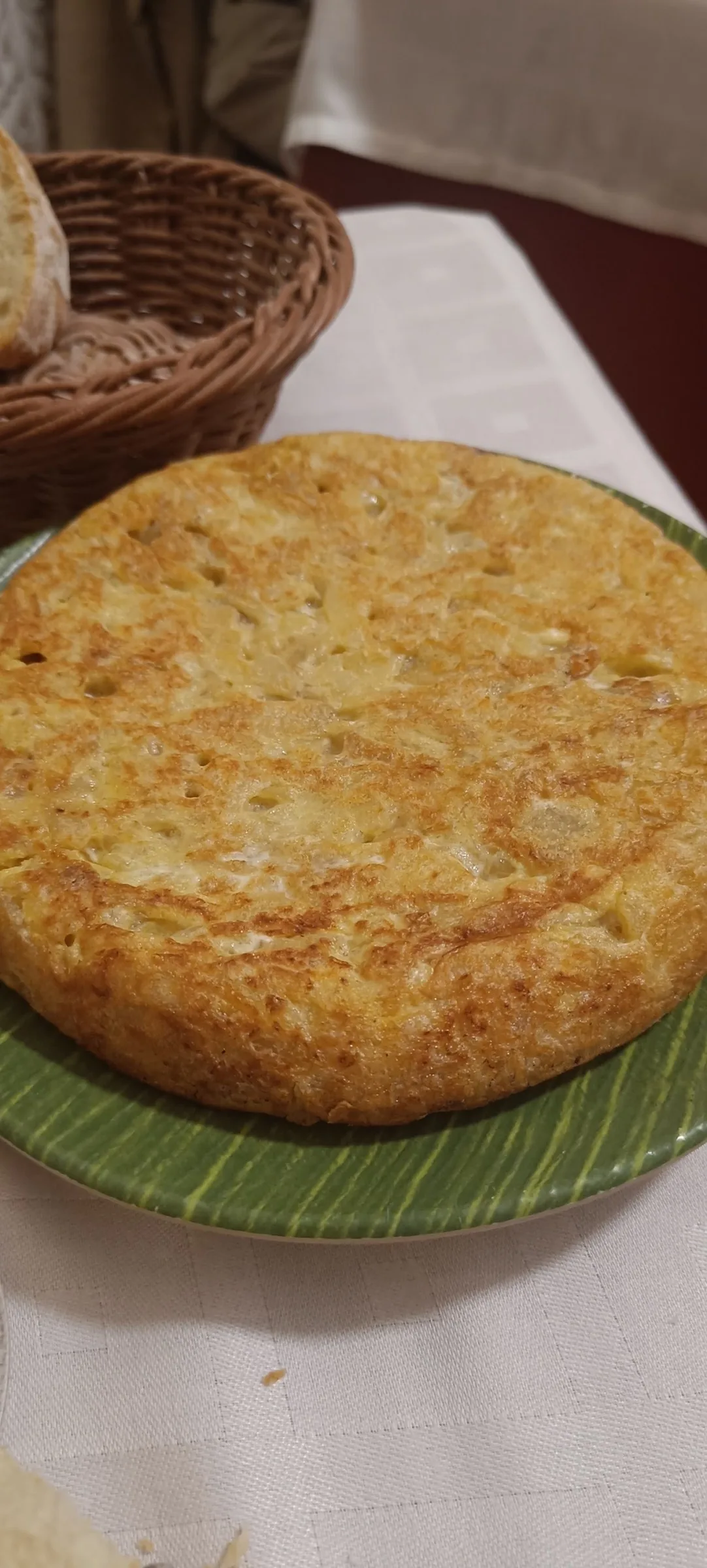 A round golden potato omelette on a green plate beside a bread basket