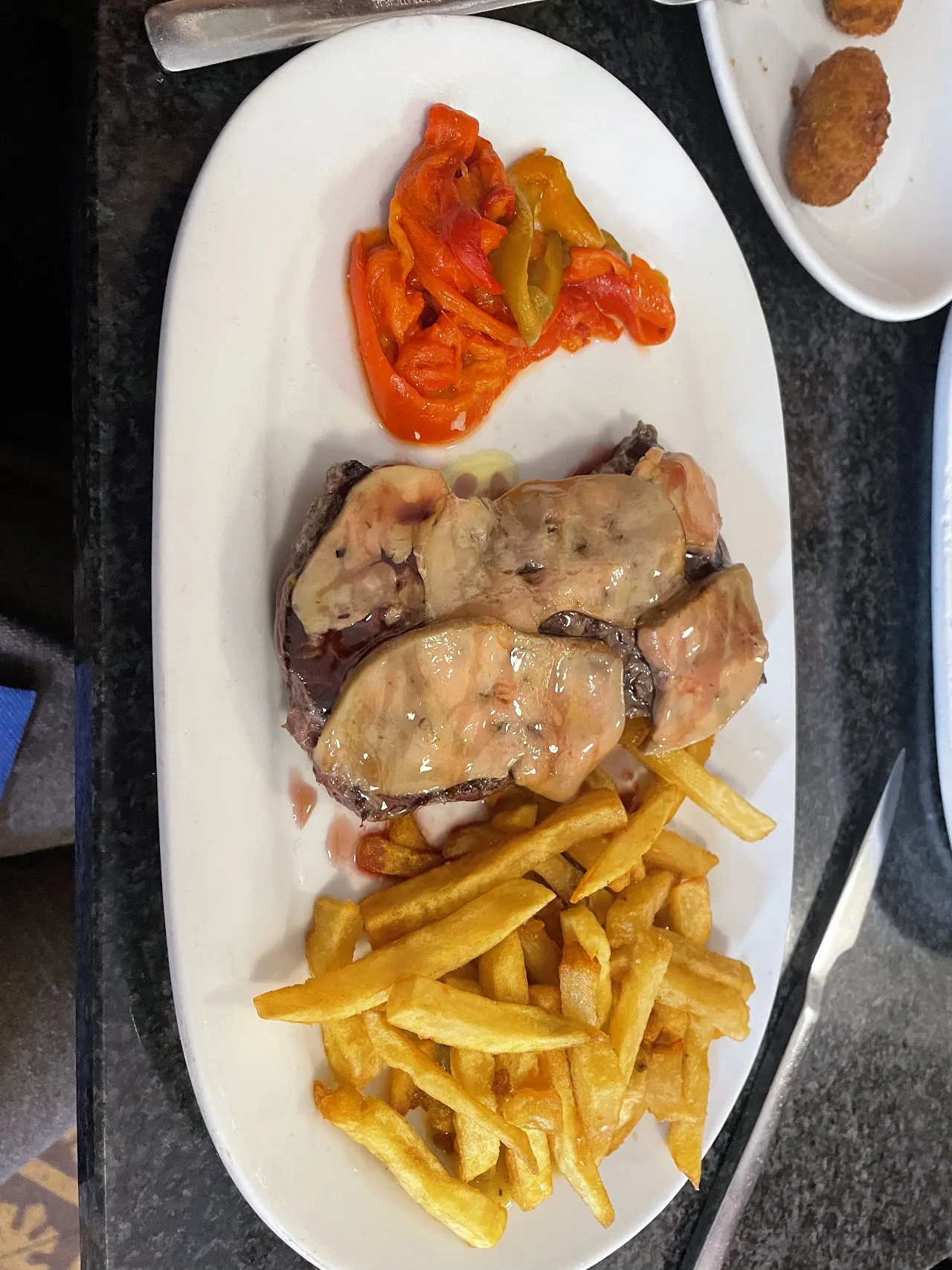 A platter of grilled meat with roasted red peppers and french fries
