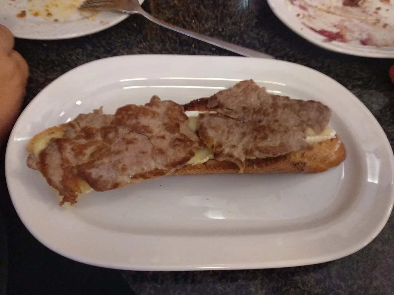An open sandwich topped with sliced meat and melted cheese