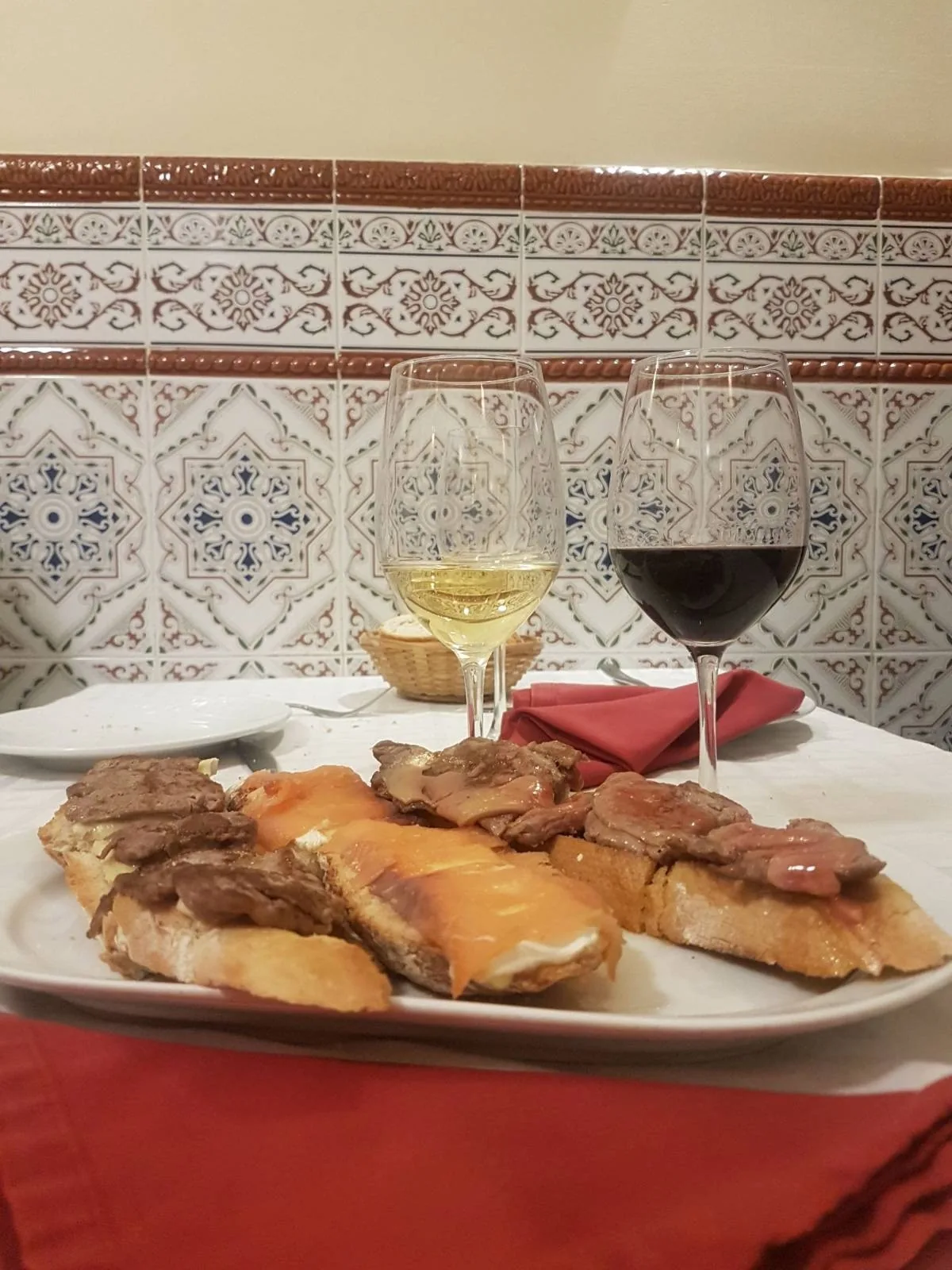 A plate of toasts topped with browned meat beside glasses of white and red wine
