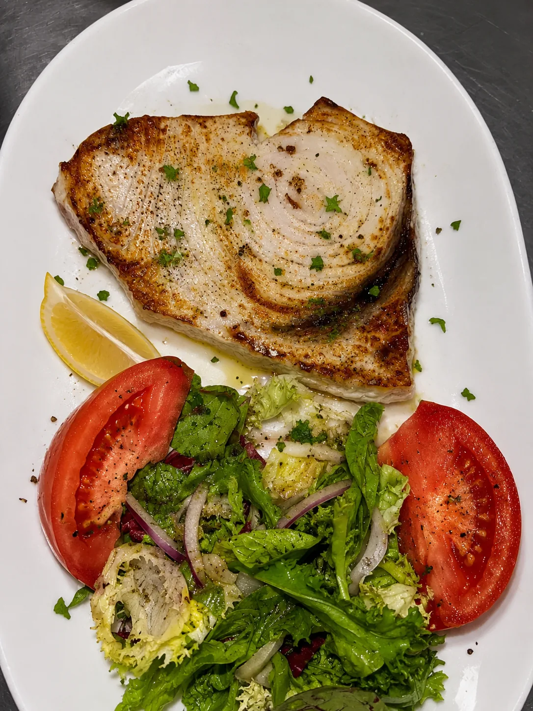A grilled whole fish fillet served with lemon and a tomato salad
