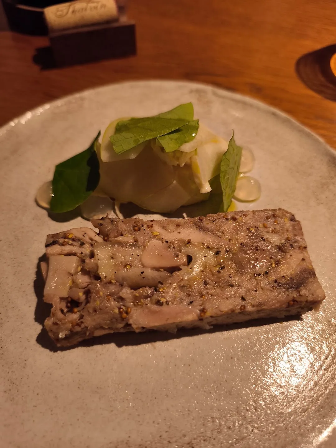 A sliced terrine topped with fresh green leaves and pale vegetable ribbons on a speckled plate