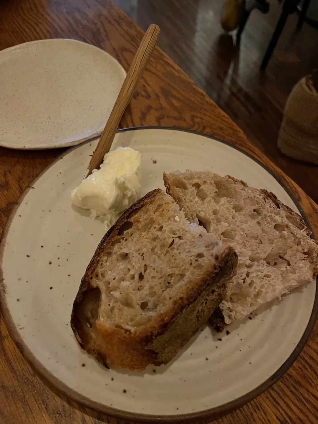 Two thick slices of crusty artisan bread beside a mound of whipped butter with a wooden knife on a ceramic plate