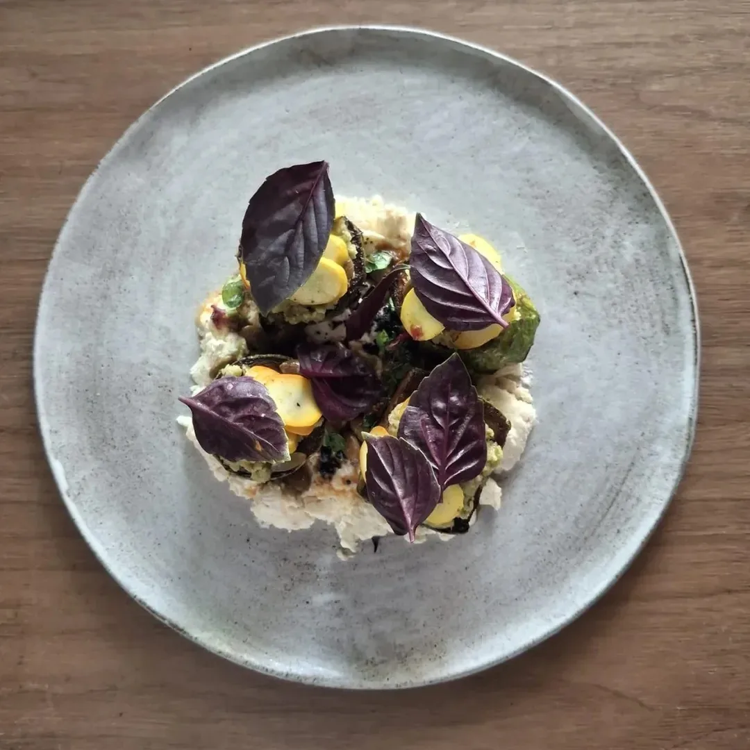 A grey plate of a grain dish topped with purple basil leaves and yellow pieces