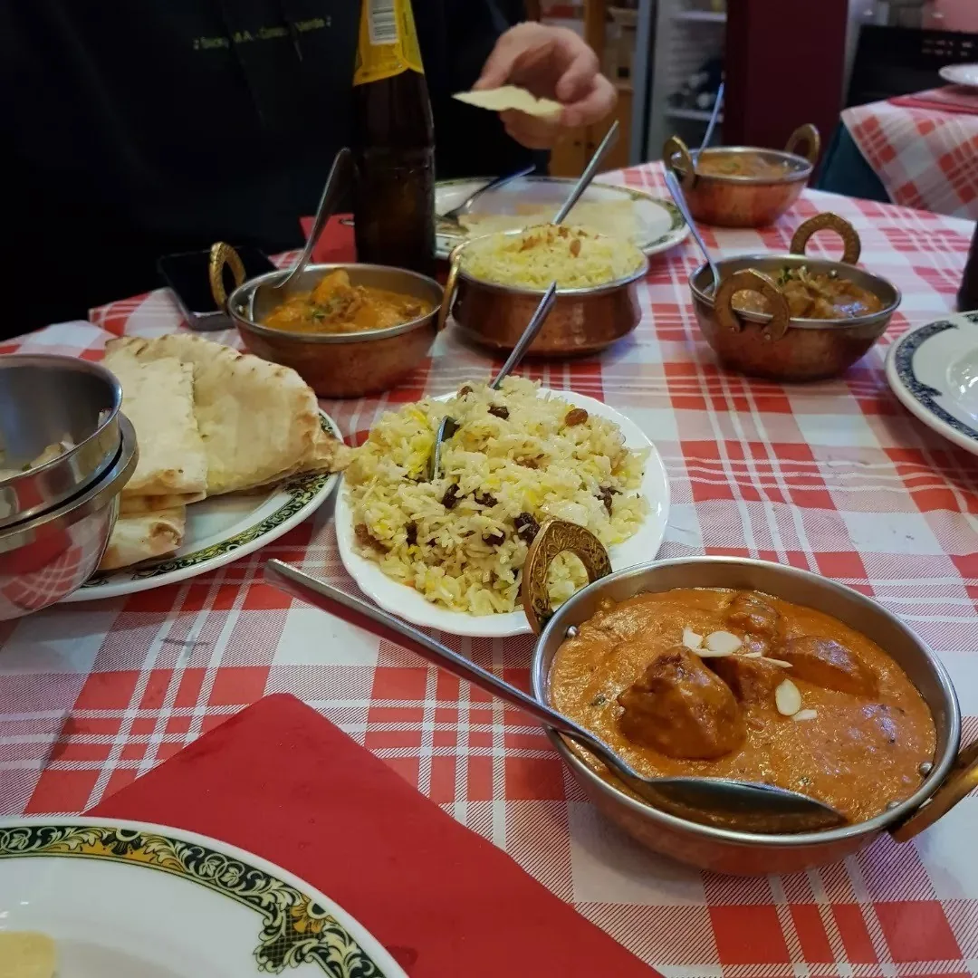 A table with copper bowls of curry, plates of rice and naan bread on a red checked tablecloth
