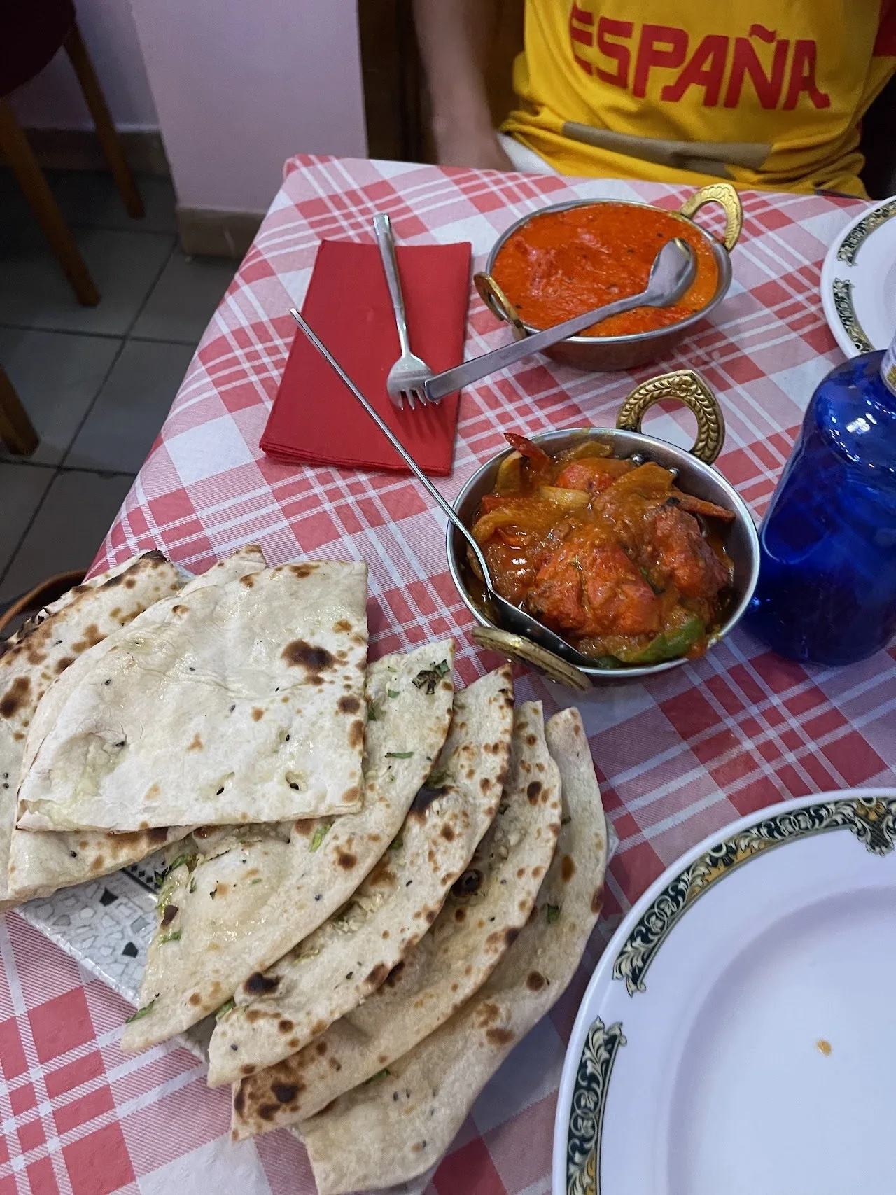 A stack of flatbreads beside bowls of orange curry on a red checked tablecloth