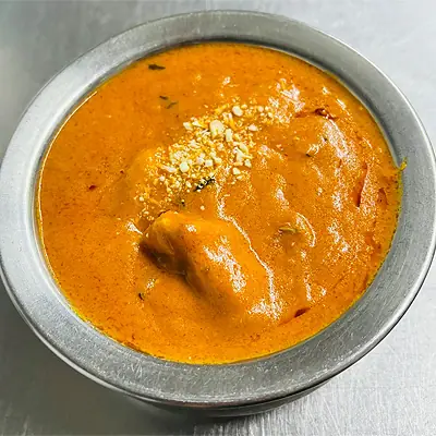 Butter chicken curry in a metal bowl, topped with a swirl of cream and crushed nuts, Bombay Spicy