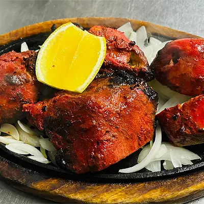 Tandoori chicken pieces charred red on a sizzling platter with sliced onions and a lemon wedge, Bombay Spicy