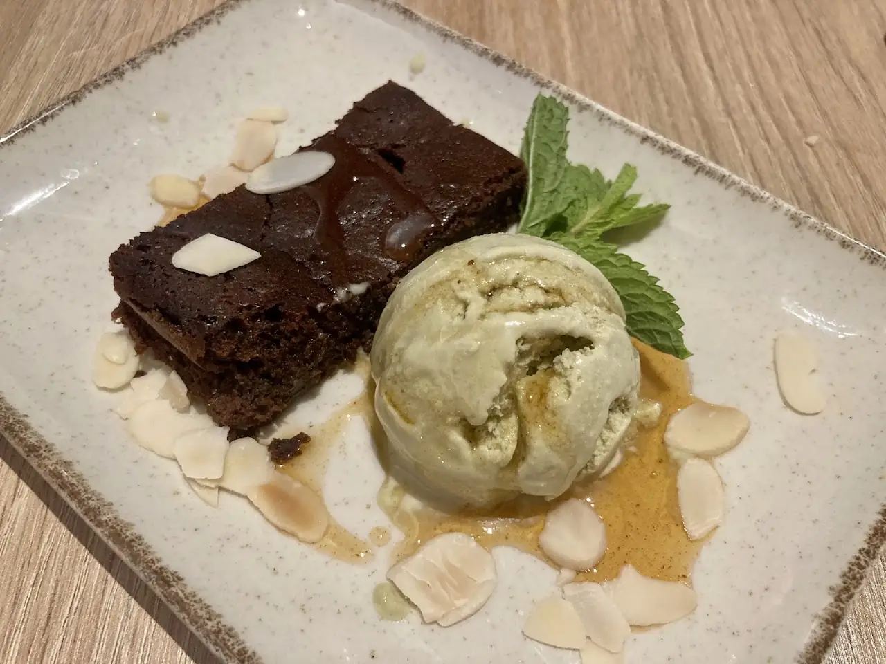 A wedge of chocolate brownie with a scoop of light green ice cream, dusted with sliced almonds.