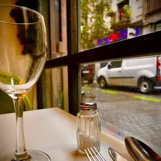 Table set by a window with a wine glass, cutlery and a glass salt shaker, looking out onto a cobbled street with a parked white van