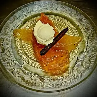 Dessert of candied citrus slices topped with a quenelle of cream and a vanilla pod on an etched glass plate