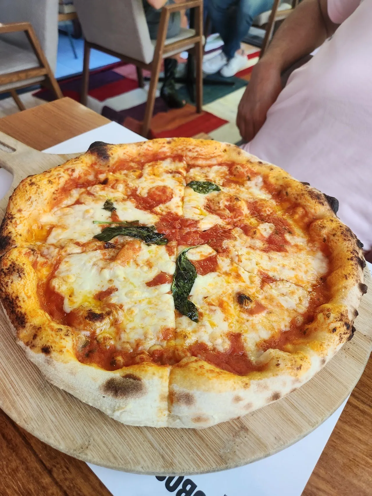 A round pizza with tomato, melted cheese and basil leaves on a wooden board