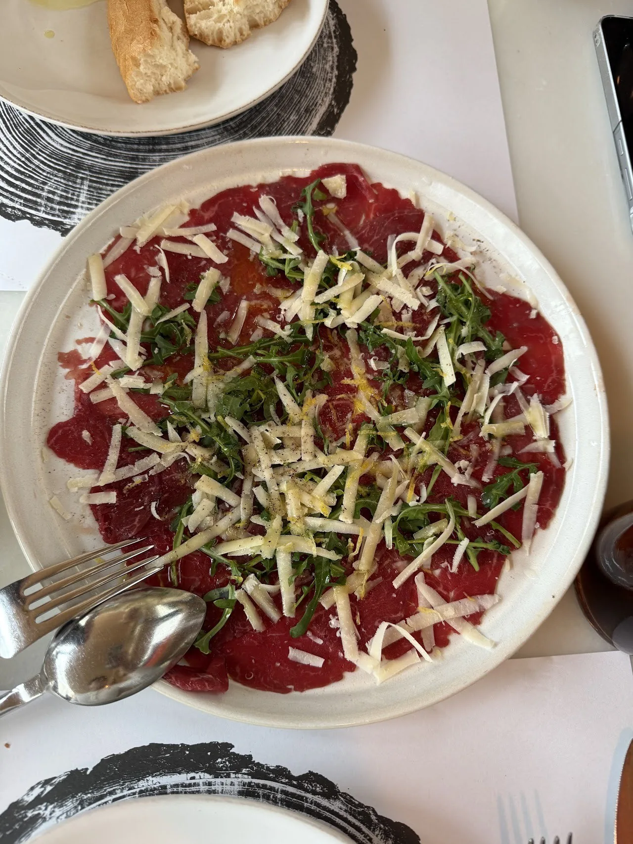 A white plate of thinly sliced raw beef topped with strips of vegetables and herbs