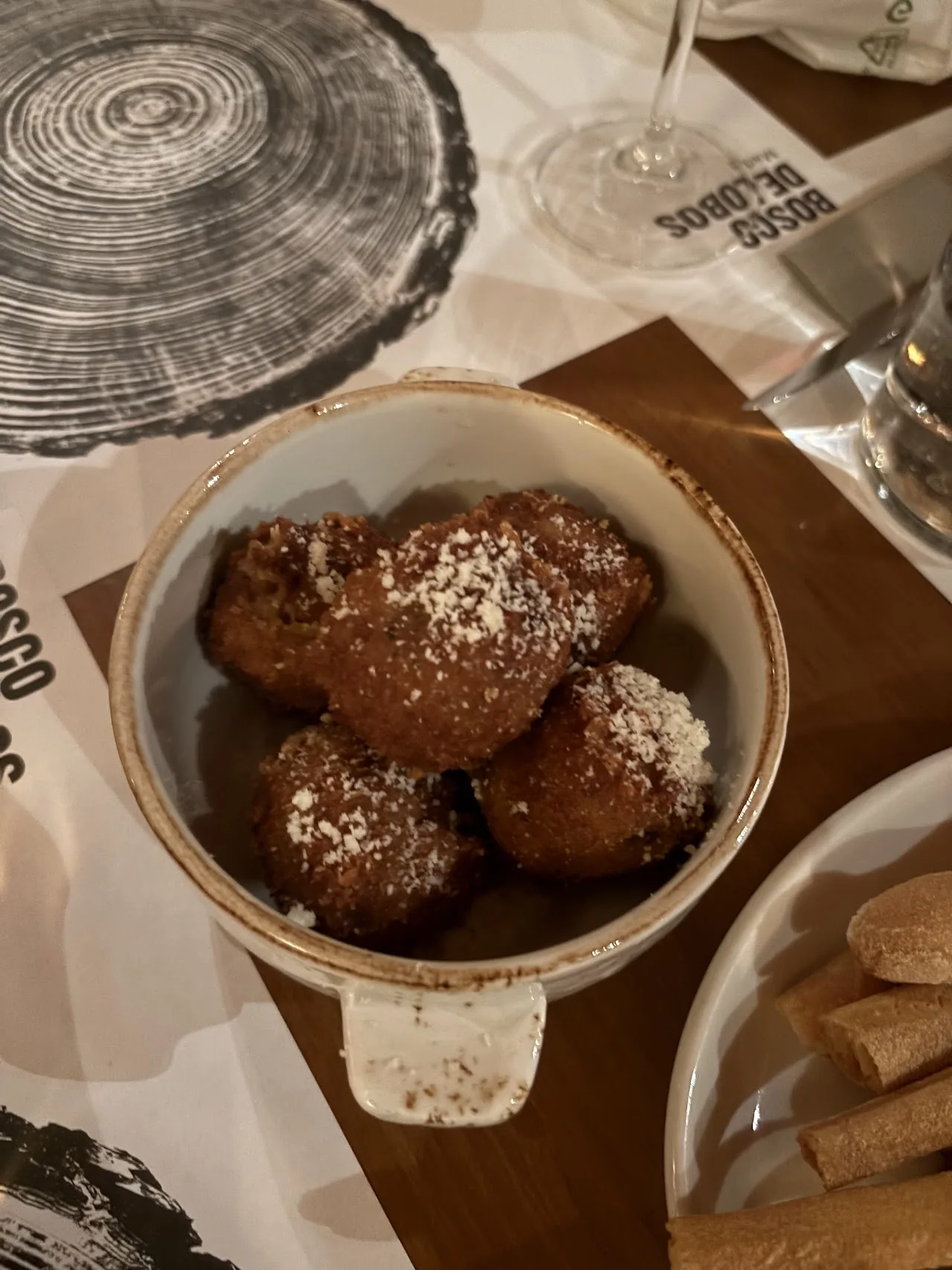 A bowl of fried dough balls dusted with powdered sugar