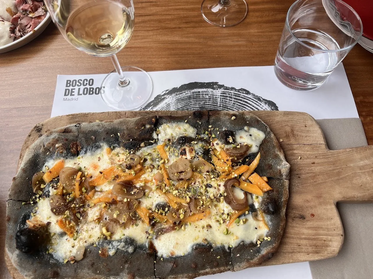 A long dark flatbread pizza with mushroom and orange toppings on a wooden board