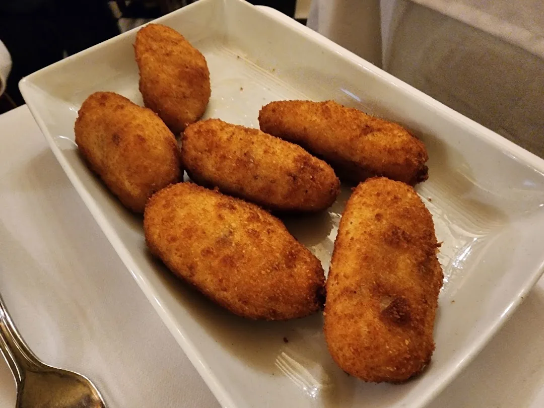 Five golden fried croquetas arranged on a white rectangular plate