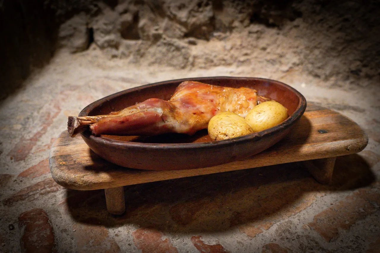 A roasted portion of meat with a potato in an oval clay dish on a wooden board