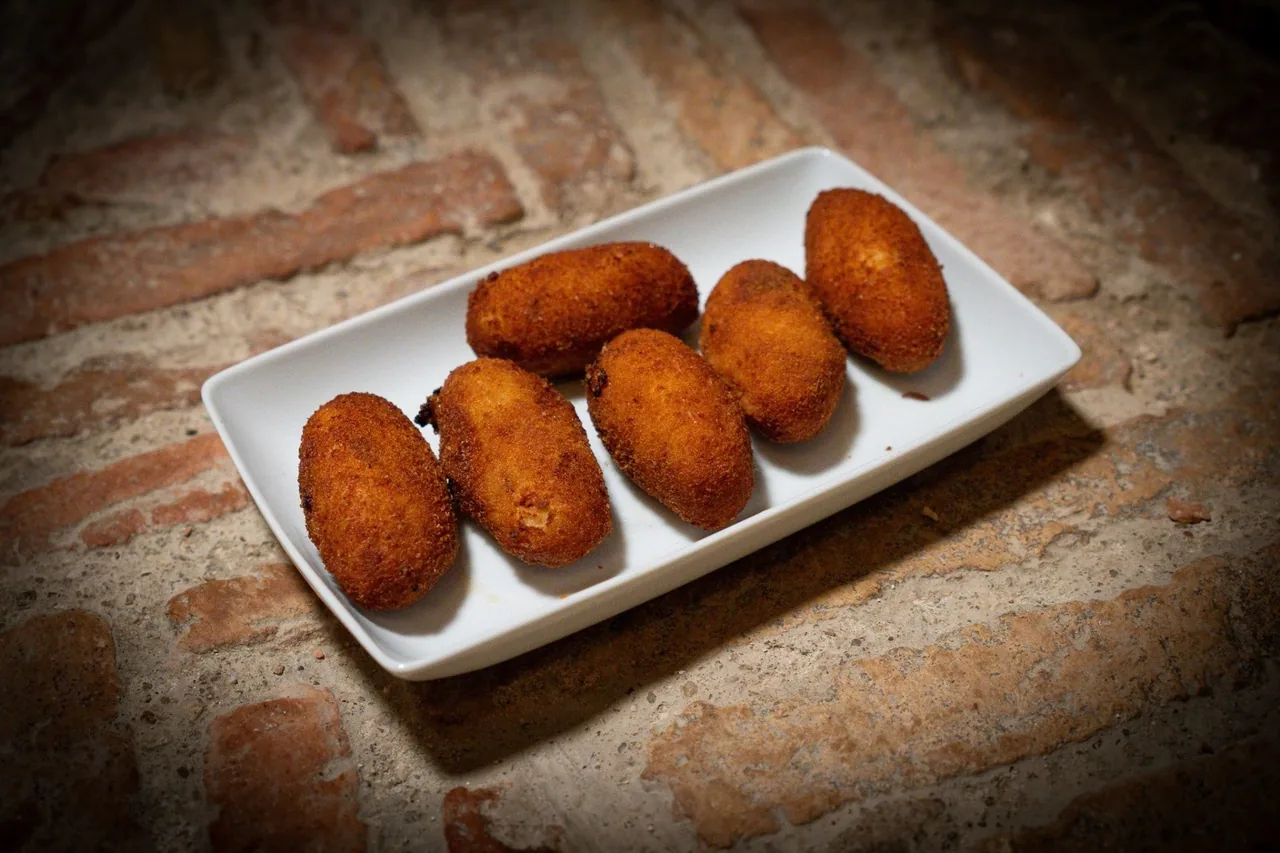 A white plate of golden croquetas on a brick-patterned surface