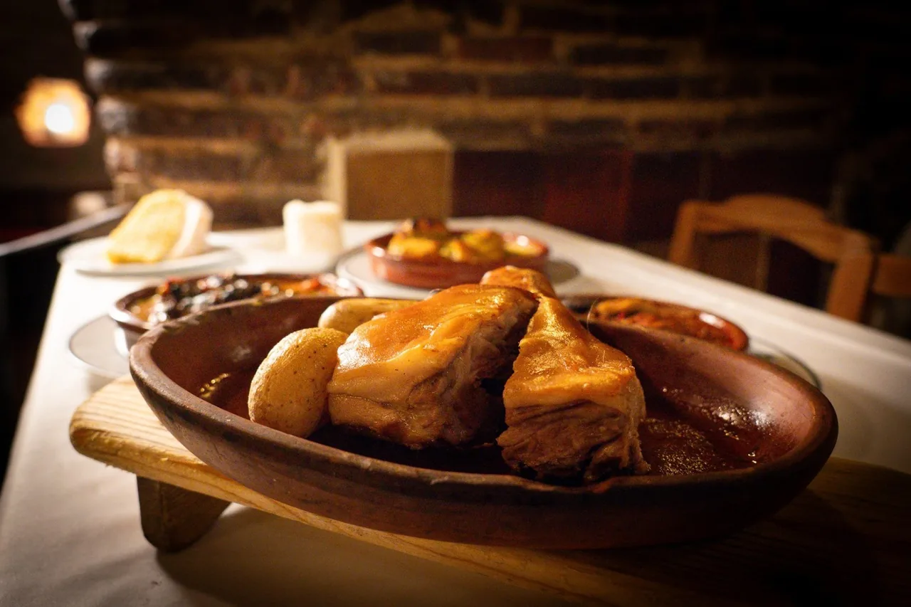 A clay dish of roast suckling pig portions with a potato on a set table