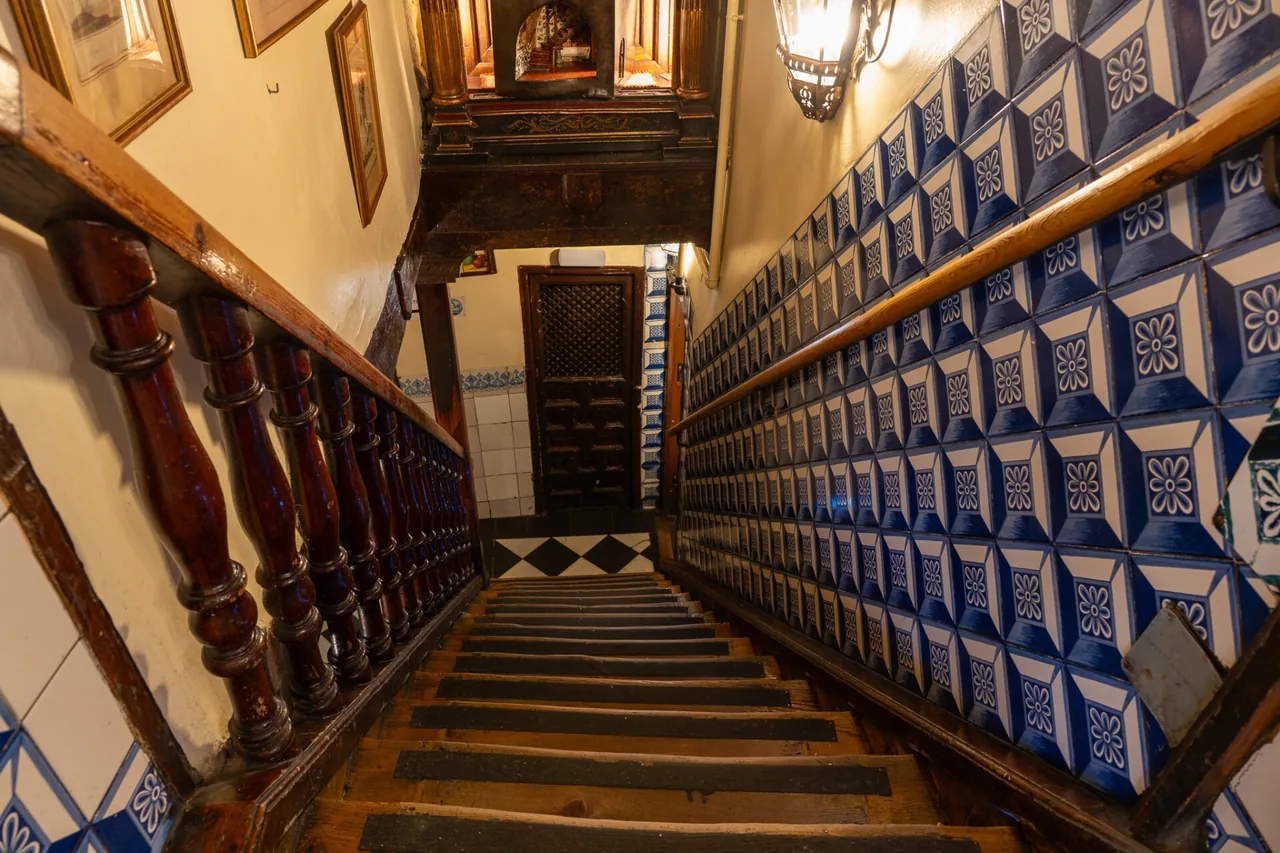 A staircase with a wooden banister running beside a wall of blue and white tiles.