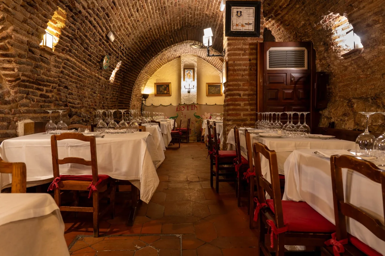 A vaulted brick dining room with white-clothed tables and red cushioned chairs