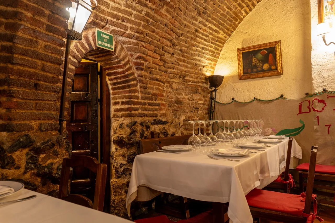 A brick alcove with a long set table with upturned glasses and a framed painting