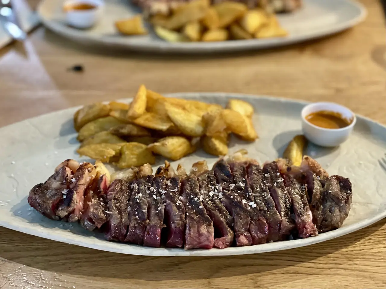 Sliced grilled steak with salt crystals, potato wedges and a sauce cup
