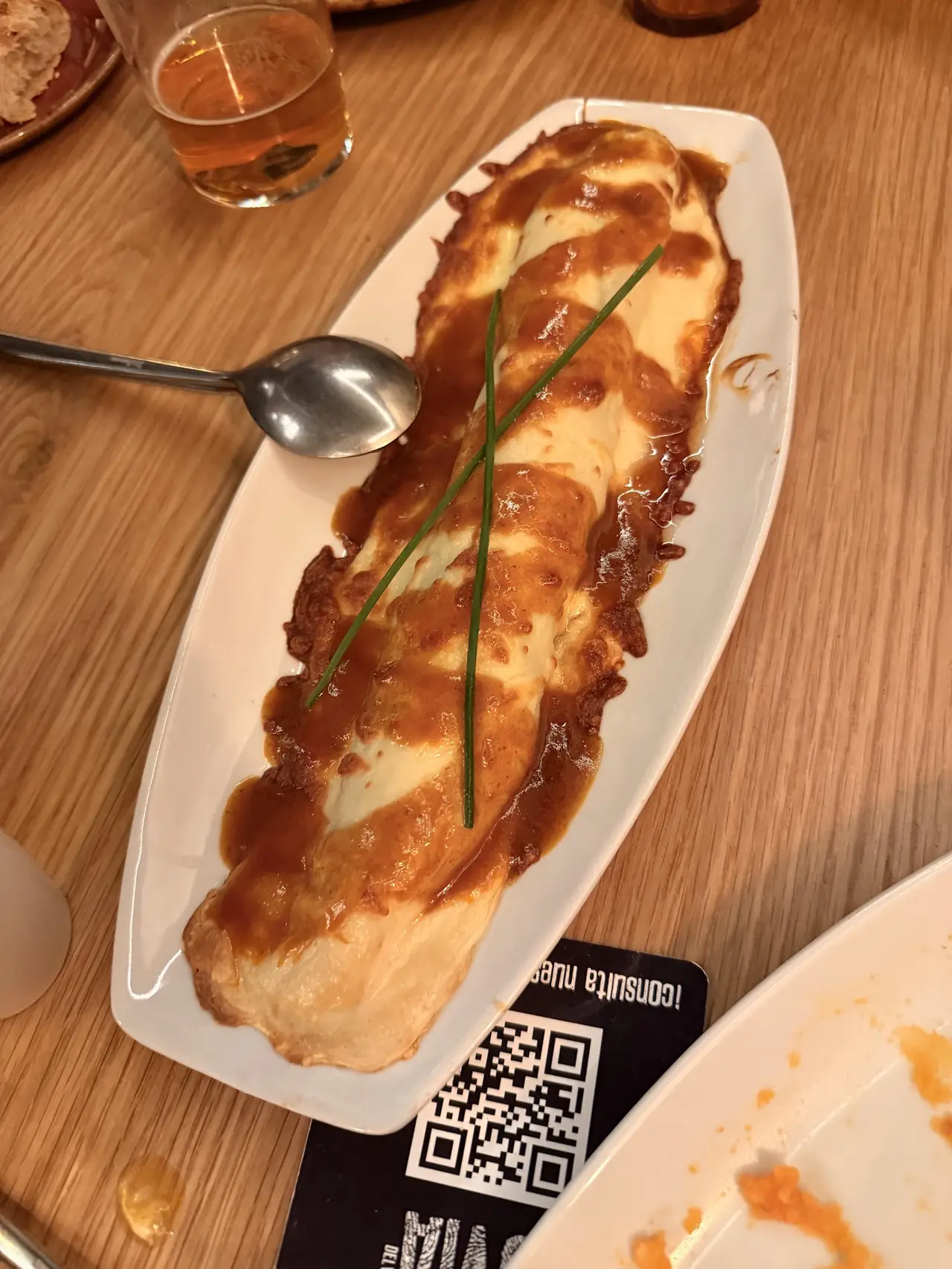 Baked cheese-topped dish with brown sauce and chive garnish on an oval plate
