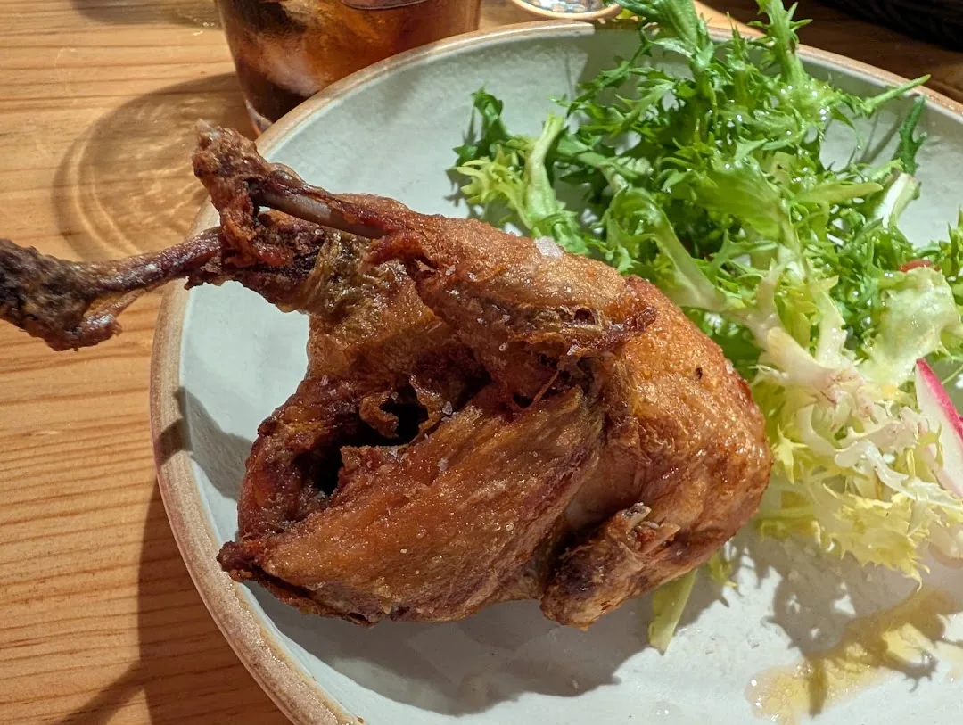 A fried quail leg with crispy skin plated alongside frisee and radish