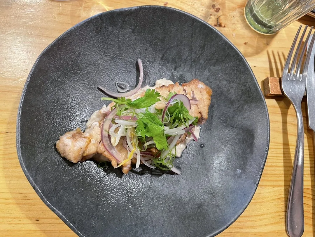 A pork dish topped with pickled red onion, cilantro, and scallion in a dark ceramic bowl
