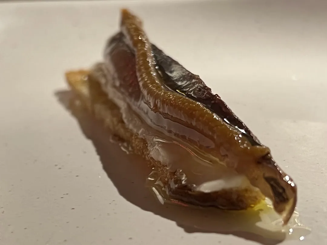 A close-up of a glossy, marinated fish fillet drizzled with oil on a white plate