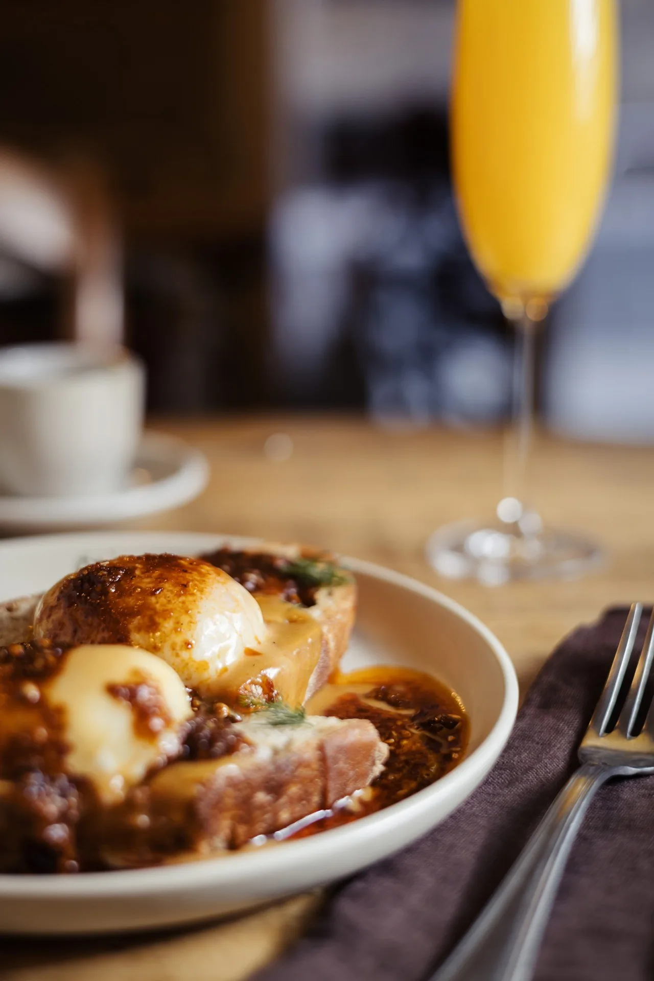A plate of eggs and meat beside a tall glass of sparkling orange drink on a wooden table