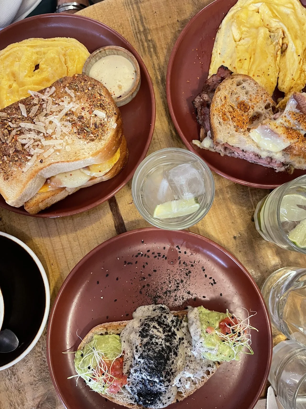 A wooden table with plates of toasted sandwiches and a toast topped with avocado