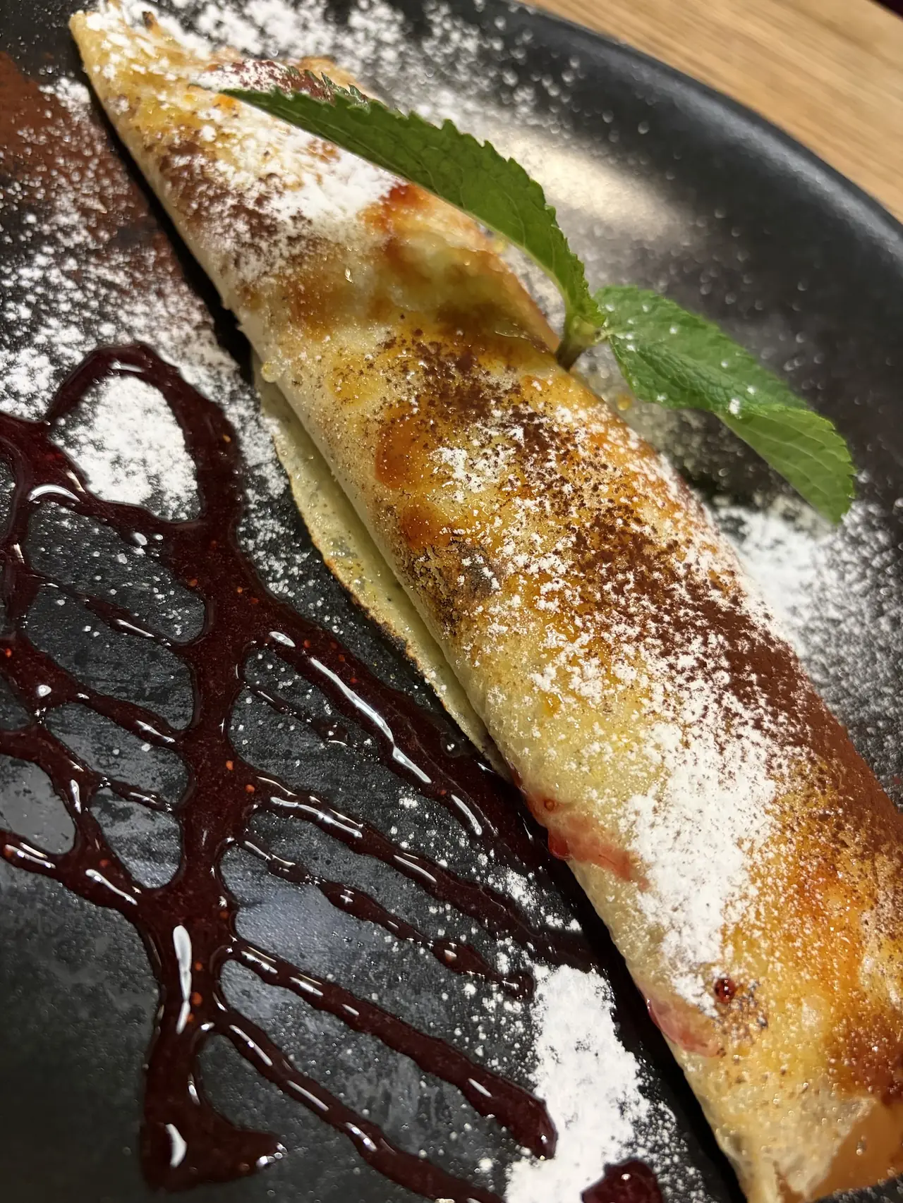 A rolled pancake dusted with sugar beside a chocolate drizzle