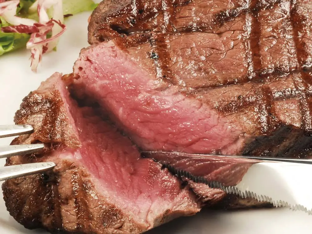 Grilled ribeye steak sliced open to show a pink center, served with a small green salad on a white plate at Buenos Aires Grill Restaurant