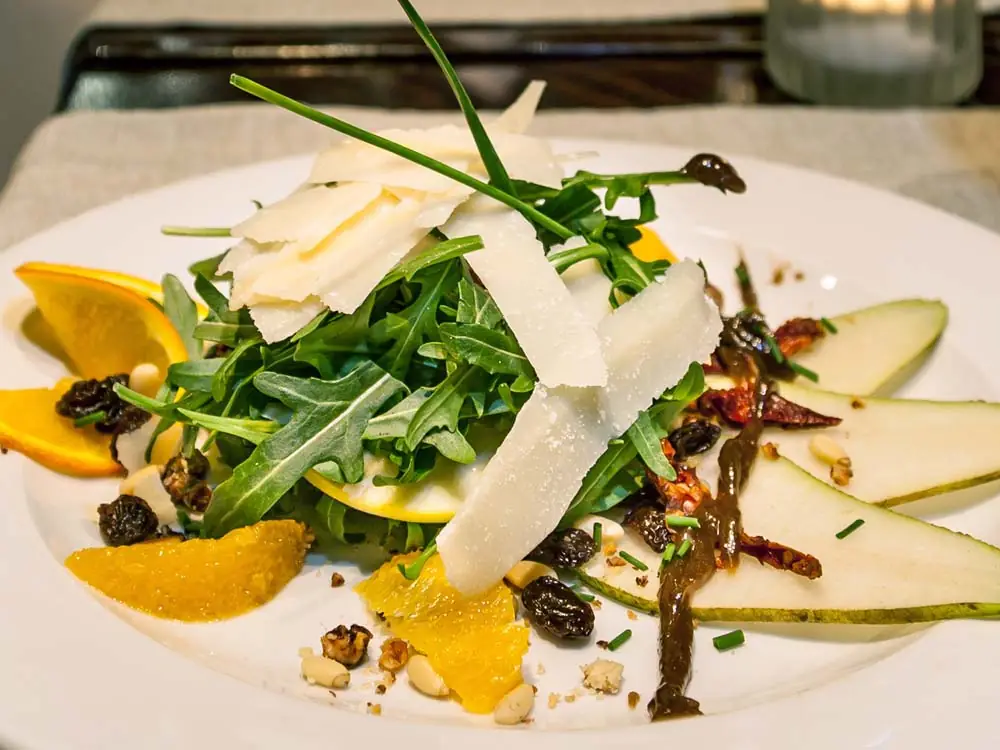 Arugula salad topped with shaved parmesan, orange segments, pear slices, raisins, and nuts with a balsamic drizzle at Buenos Aires Grill Restaurant