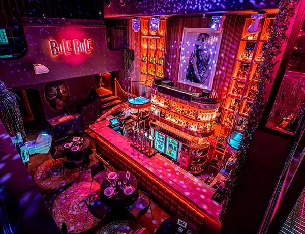 Overhead view of a red-and-purple lit club interior with a central curved bar, neon Bule Bule sign and lounge tables