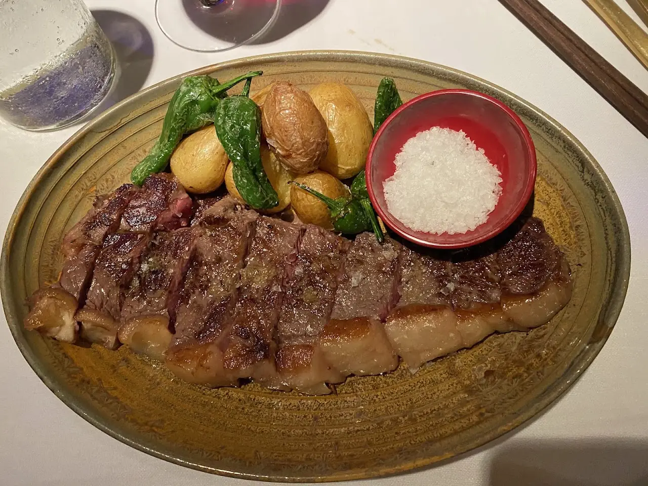 A grilled steak sliced on a plate with roasted baby potatoes and a small bowl of rice.