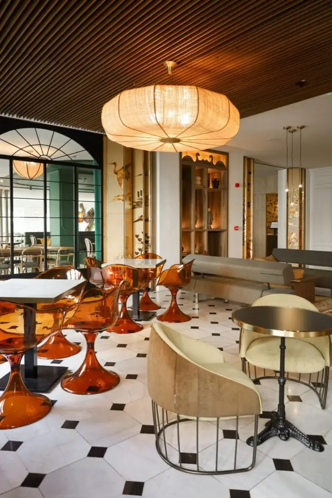 Stylish dining room with translucent amber tulip chairs, marble-top tables, a large woven pendant lamp and black-and-white diamond floor tiles