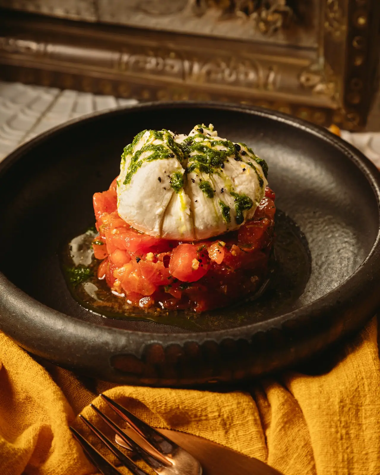 Burrata cheese set over sliced tomatoes on a dark plate.