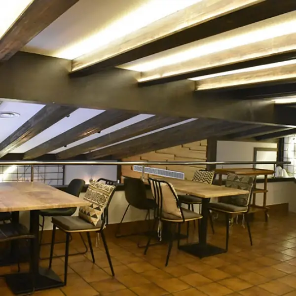 Upper dining area with exposed wood ceiling beams, light wood tables, patterned-cushion chairs and terracotta tile floor
