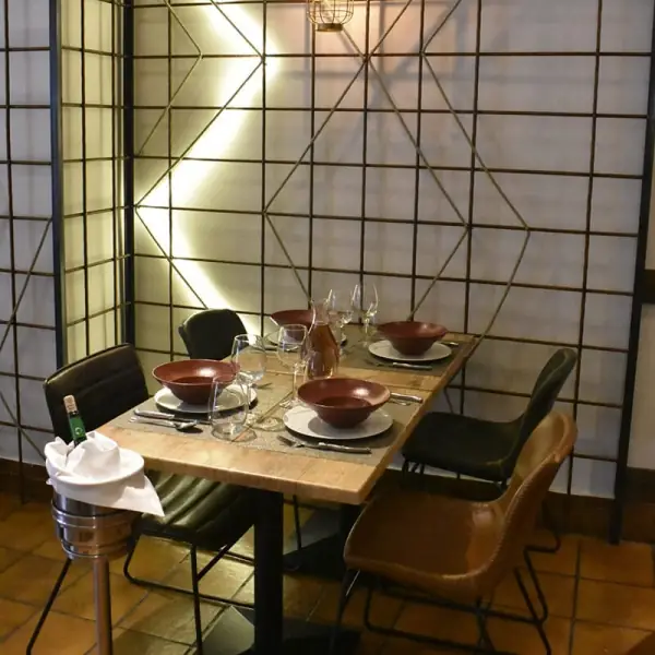 Corner table set with red bowls, wine glasses and cutlery against a lit geometric lattice wall