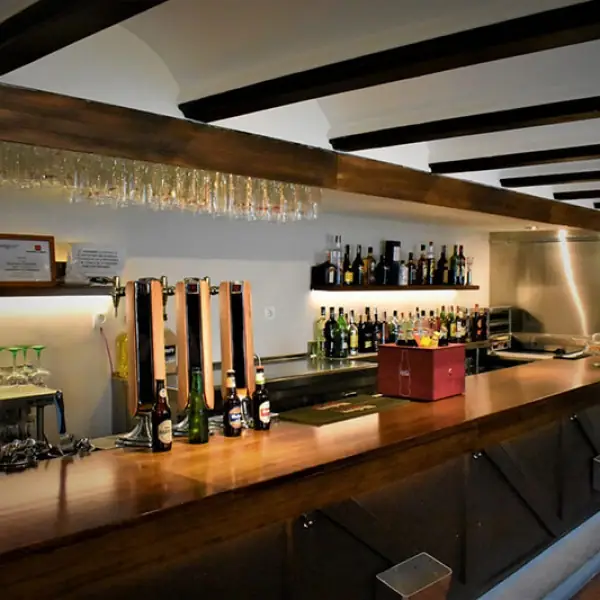 Wooden bar counter with beer taps, bottles of beer and a back shelf of spirits under hanging glassware