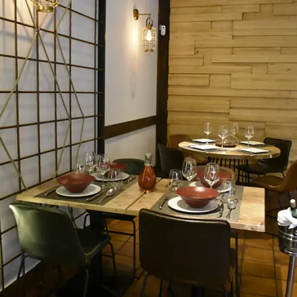 Dining tables set with red bowls, wine glasses and place settings beside a wood-panelled wall and lattice screen