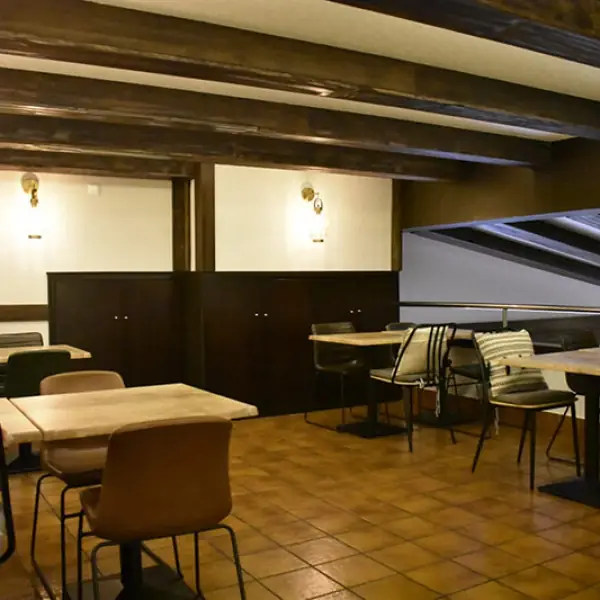 Dining room with wood ceiling beams, dark cabinetry, light wood tables and leather chairs on terracotta tiles