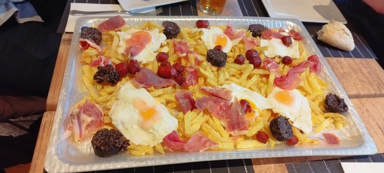 A large tray of fries topped with fried eggs, slices of cured ham, black pudding and small chorizos